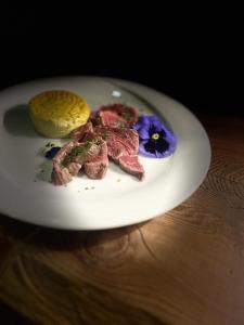 a white plate with meat and a purple flower on it at Hotel Rio Bianco in Panchià
