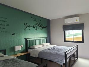 a bedroom with two beds and a green wall at บ้าน ชลรพี Baan Chonrapee in Ban Pak Nam Krasae