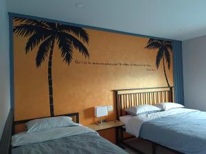 een slaapkamer met 2 bedden en een muurschildering van palmbomen bij บ้าน ชลรพี Baan Chonrapee in Ban Pak Nam Krasae