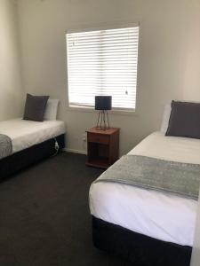 a bedroom with two beds and a window and a table at Rosetown Motel in Te Awamutu