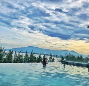 a woman in a swimming pool with mountains in the background at Santori Hotel Da Nang Bay in Da Nang