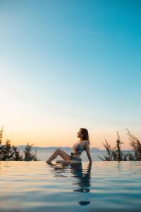 a woman sitting on the edge of a swimming pool at Santori Hotel Da Nang Bay in Da Nang