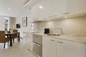 a kitchen with white cabinets and a sink and a table at 119 Santai Resort - Poolside Apartment by uHoliday in Casuarina