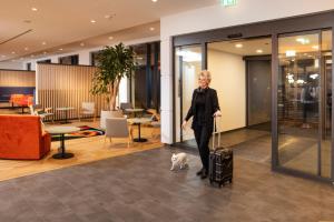 a woman with her luggage and a dog in a lobby at LOGINN Hotel Berlin Airport in Berlin