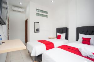 two beds in a room with white walls and red pillows at RedDoorz at Jalan Bangau Palembang in Palembang