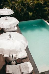 two white umbrellas sitting next to a swimming pool at The Room Padang-Padang in Uluwatu