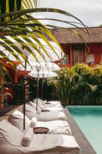 a row of white lounge chairs with umbrellas next to a pool at The Room Padang-Padang in Uluwatu