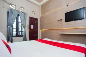 a bedroom with a white bed and a flat screen tv at RedDoorz at KM 5 Palembang in Palembang