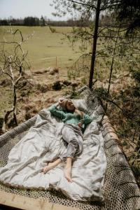 a woman laying on a hammock in a field at Nature calls - tree tents in Būtingė