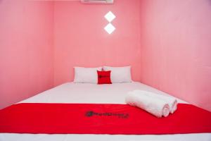 um quarto rosa com uma cama branca e um cobertor vermelho em RedDoorz near Simpang Bandara SMB II em Palimbão