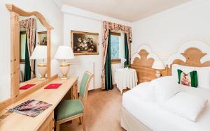 a bedroom with a white bed and a desk with chairs at Hotel Sassongher in Corvara in Badia