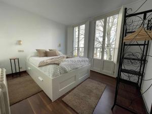 a white bedroom with a bed and a large window at A morada das perseidas in Ourense