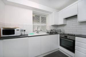 Biała kuchnia z białymi szafkami i kuchenką mikrofalową w obiekcie Ealing Garden Flat w mieście Ealing