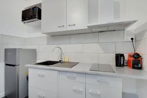 La cuisine blanche est équipée d'un évier et d'un réfrigérateur. dans l'établissement Cosy appartement aux Portes de Paris, à Aubervilliers