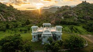 an aerial view of a building in a field with mountains at amã Stays & Trails Abhay Manor Kaali Toonk, Udaipur in Ghānerao