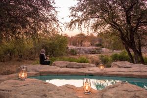 a person sitting on a rock near a pool of water at Simbavati River Sands in Timbavati Game Reserve