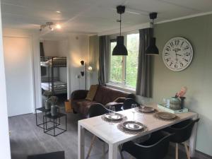 a living room with a table and a clock on the wall at Vacare chalet in Drijber