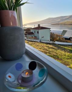 a candle on a window sill with a view of a house at Summarhús29 in Tvøroyri
