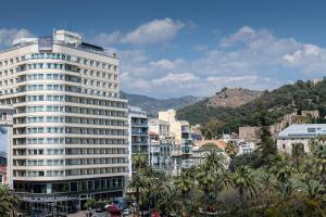 een hoog wit gebouw in een stad met palmbomen bij AC Hotel Málaga Palacio by Marriott in Málaga