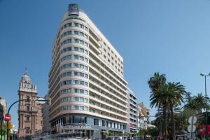 een hoog wit gebouw in een stadsstraat met palmbomen bij AC Hotel Málaga Palacio by Marriott in Málaga