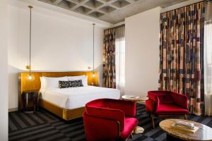 インディアナポリスにあるHotel Indy, Indianapolis, a Tribute Portfolio Hotelのベッド1台と赤い椅子2脚が備わるホテルルームです。