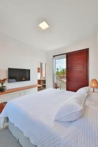 a white bedroom with a large bed and a tv at Pousada Praia do Patacho in Pôrto de Pedras