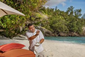 a man standing on a beach next to an umbrella at North Island, a Luxury Collection Resort, Seychelles in North Island