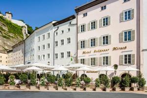 ein großes weißes Gebäude mit Tischen und Sonnenschirmen in der Unterkunft Hotel Goldener Hirsch, A Luxury Collection Hotel, Salzburg in Salzburg