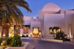 Al Wathba, a Luxury Collection Desert Resort & Spa, Abu Dhabi في أبوظبي: مبنى ابيض كبير امامه نخلة