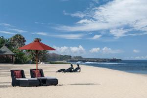 two people sitting on the beach under an umbrella at The St. Regis Bali Resort in Nusa Dua