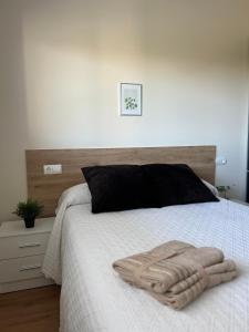 a bed with a black pillow and two towels on it at Costa Santander. Apartamento con jardín in Santander