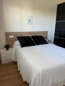 una camera da letto con un grande letto bianco con cuscini neri di Costa Santander. Apartamento con jardín a Santander