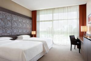 Fernoにあるシェラトン ミラン マルペンサ エアポート ホテル ＆ カンファレンス センターのベッド2台、デスク、窓が備わるホテルルームです。