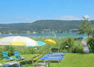 un grupo de sillas y sombrillas en el césped en Ferienwohnung Schellander Privatstrand en Velden am Wörthersee