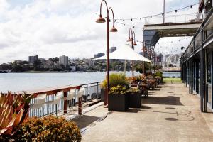 a patio with tables and an umbrella next to the water at Pier One Sydney Harbour, Autograph Collection in Sydney