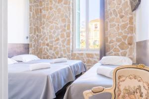 a room with three beds and a chair and a window at Hotel De Belgique à Menton in Menton