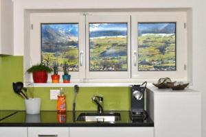 a kitchen with a sink and two windows with mountains at Seeblick - a78060 in Stalden