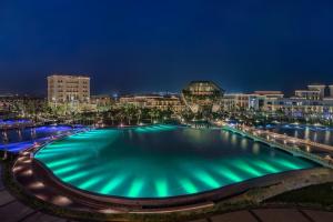 una gran piscina con luces verdes en una ciudad por la noche en The St Regis New Capital Cairo en El Cairo