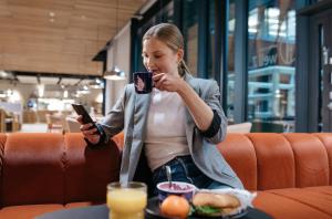 una mujer sosteniendo un celular mientras se sienta en una mesa en Heymo 1 by Sokos Hotels en Espoo