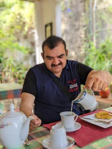 een man die een kop koffie roert aan een tafel bij Kandy IVY Banks Holiday Resort in Kandy