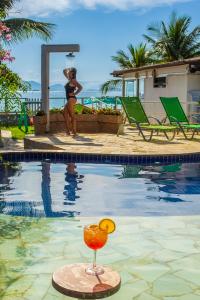 a woman standing next to a swimming pool with a drink at Pousada Daleste in Angra dos Reis