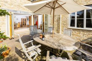a wooden table and chairs with an umbrella on a patio at Little Maunditts Cottage - quiet location in charming Cotswold village in Sherston