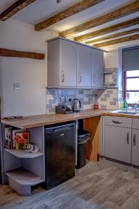 a kitchen with white cabinets and a black dishwasher at Forget me not cottage in Ironbridge