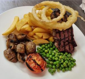 un plato de comida con filete, aros de cebolla y guisantes en The Sportsmans Inn Limited, en Ivybridge