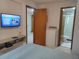 a bedroom with a television on the wall and a bathroom at Lindo Flat frente praia in Vila Velha