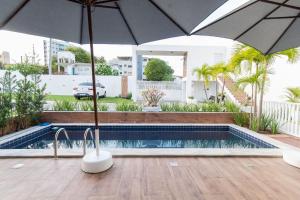 a swimming pool with an umbrella next to a house at Tríplex para 9 pessoas na cobertura do Pirangi Prime por Carpediem in Parnamirim