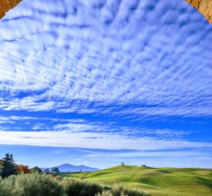 een bewolkte hemel boven een groen veld met een heuvel bij Podere Spedalone in Pienza