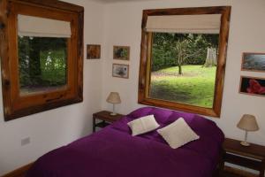 1 dormitorio con 1 cama de color púrpura y 2 ventanas en Casa en el bosque de Puerto Manzano en Villa La Angostura