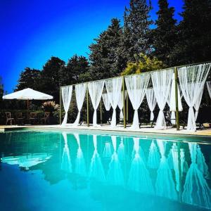 einen Pool mit weißen Vorhängen, einem Tisch und einem Sonnenschirm in der Unterkunft Mas de la Fontaine in Sarrians