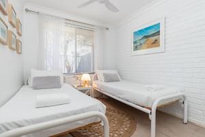 two beds in a white room with a window at The Reef in Boomerang Beach